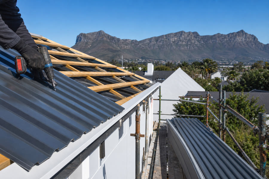 IBR sheeting being screwed onto purlins on a new Somerset West roof, scaffold and Helderberg behind.
